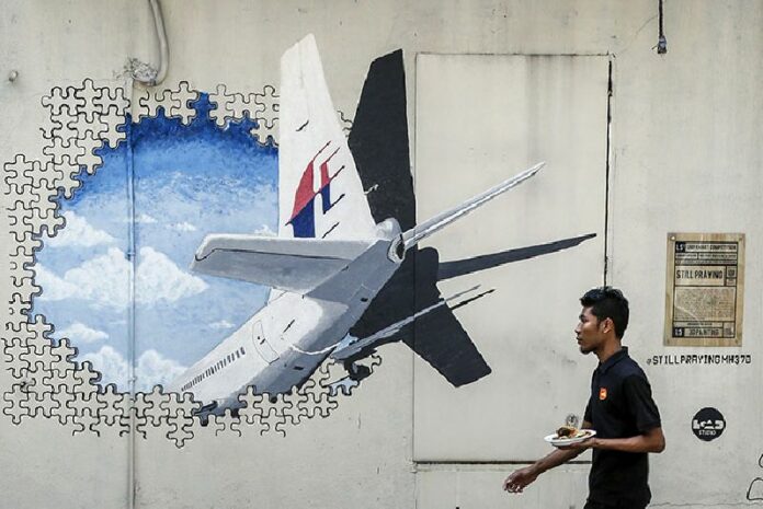 A waiter walks past a mural of Malaysia Airlines Flight 370 outside Kuala Lumpur, Malaysia, on Feb. 23. Photo: Joshua Paul / Associated Press<br />