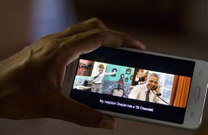 A woman poses for a photo, holding her cell phone that shows a frame from the video released by the White House of President Barack Obama joking with Cuban comedian Panfilo, in Havana, Cuba, Saturday, March 19, 2016. Photo: Ramon Espinosa / Associated Press<br />