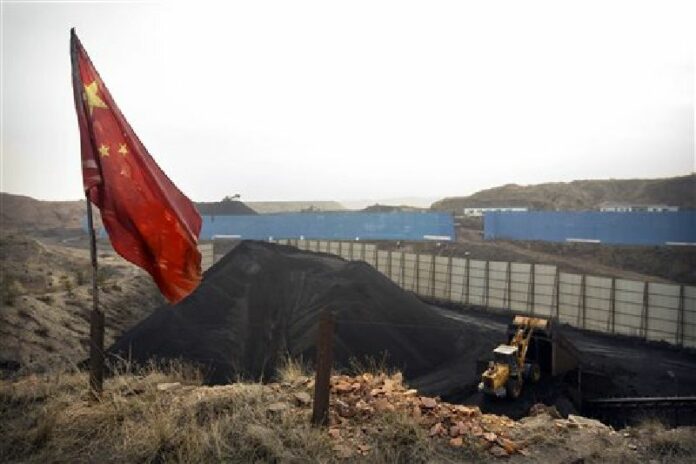 In this Nov. 4, 2015 photo, a Chinese flag stands in the breeze as a loader moves coal at a coal mine near Ordos in northern China's Inner Mongolia Autonomous Region. Photo: Mark Schiefelbein / Associated Press