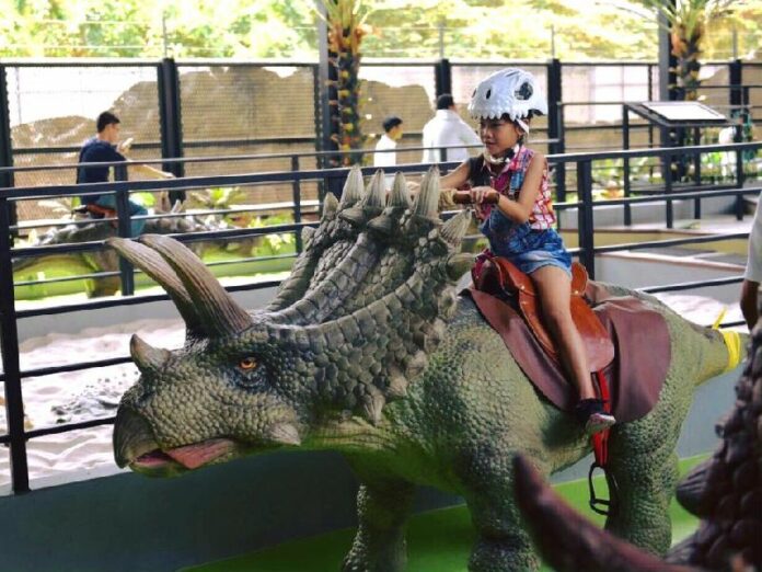 A girl rides a triceratops Friday morning at Dinosaur Planet’s Dino Farm zone in Bangkok. Photo: Dinosaur Planet / Facebook