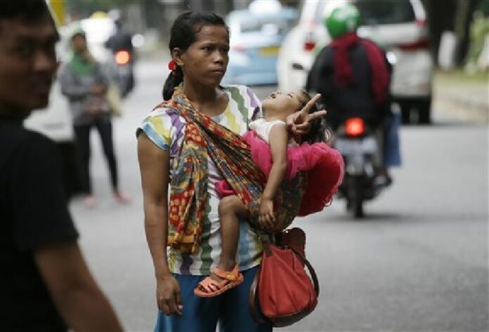In this Friday, April 1, 2016, photo, a woman carries her baby as she signals to show that she's for hire as a "jockey" to help drivers cheat a peak time traffic rule of three people to one car during rush hour, at the main business district in Jakarta, Indonesia. Photo: Achmad Ibrahim / Associated Press