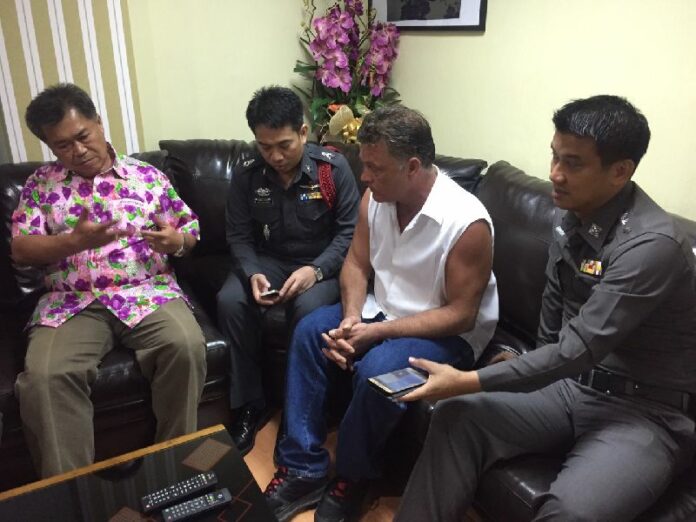 Ben Bartanyi sits with police officers Saturday at Pattaya City Police Station