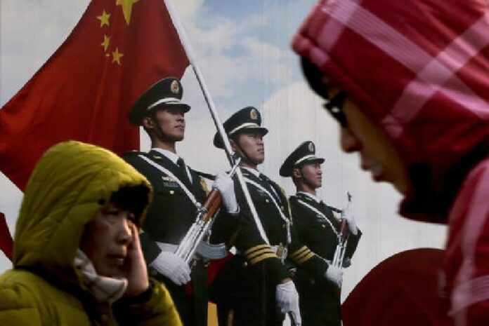 In this Jan. 21, 2016, file photo, people walk past a poster of Chinese People's Liberation Army soldiers on display in Beijing. Photo: Andy Wong / Associated Press
